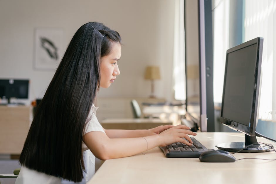 A young woman working intently on a computer in a bright, modern office setting, embodying productivity.